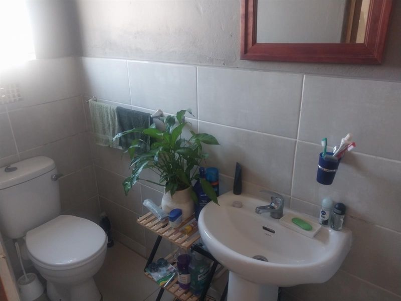 A functional bathroom featuring a pedestal basin, toilet, and neutral wall tiling, requiring minor cosmetic updates to improve the overall aesthetic.