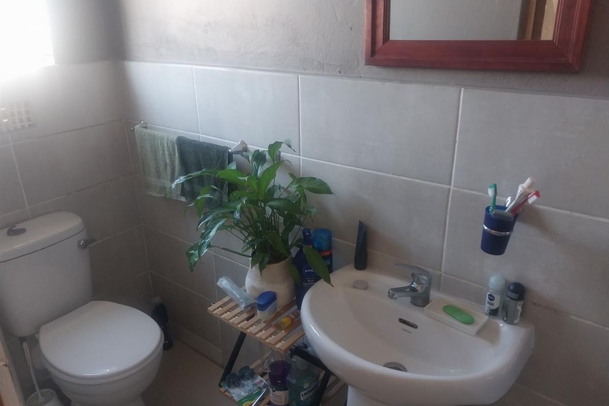 A functional bathroom featuring a pedestal basin, toilet, and neutral wall tiling, requiring minor cosmetic updates to improve the overall aesthetic.