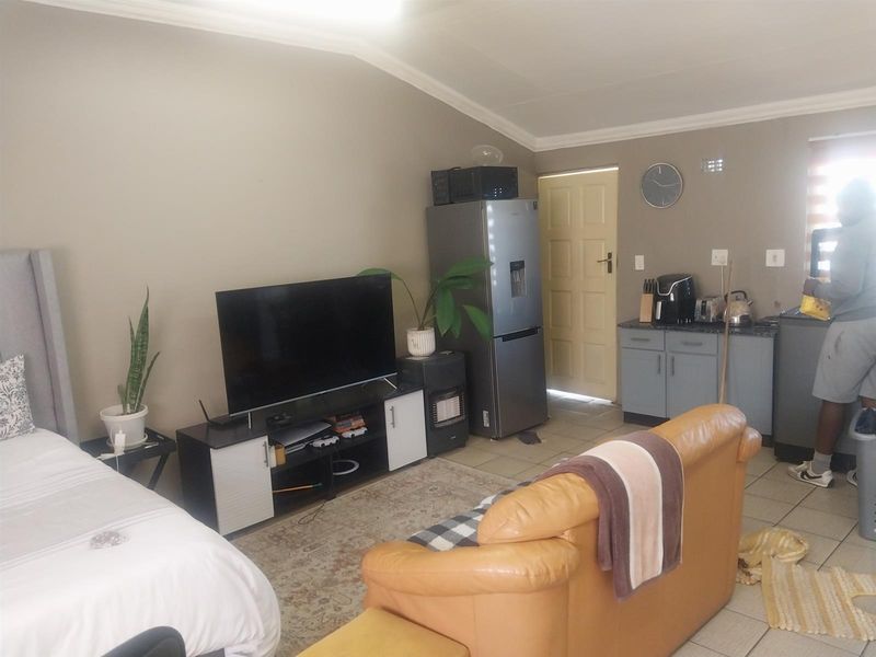 Open-plan living area featuring tiled flooring, coved ceilings, and a compact kitchenette area with built-in cabinetry and countertop space.