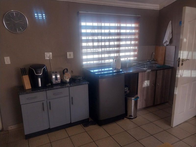 A functional kitchen area featuring built-in cabinetry, laminate countertops, a stainless steel sink, and tiled flooring with natural light from a window.