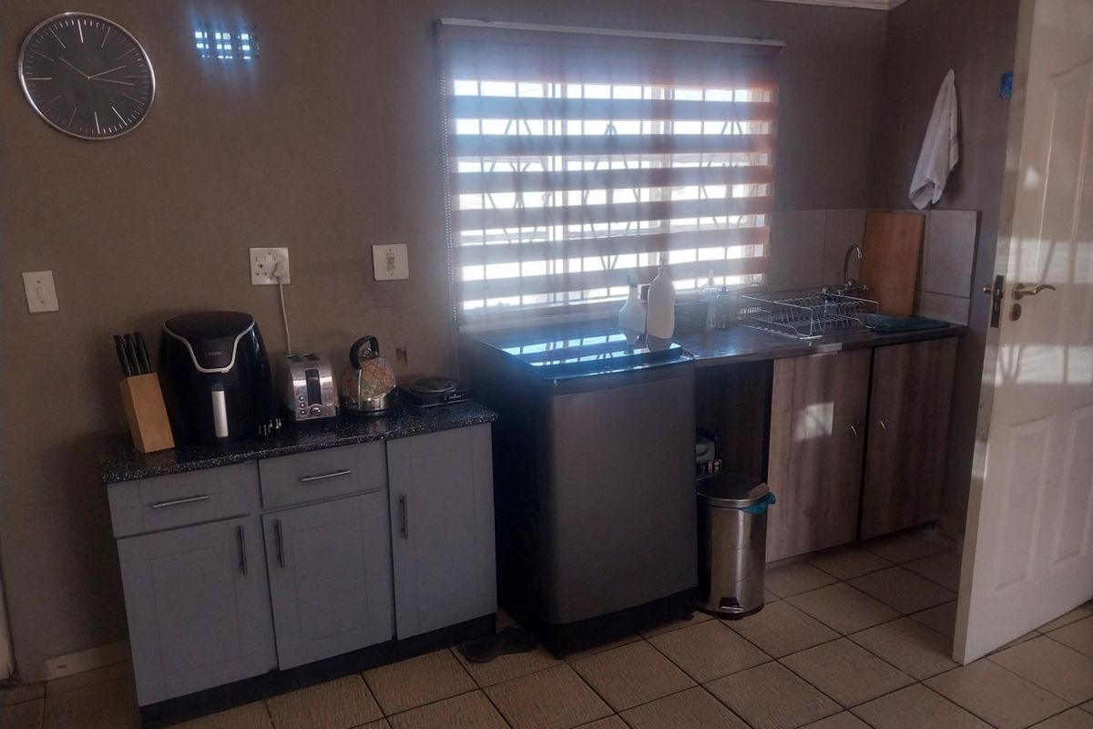 A functional kitchen area featuring built-in cabinetry, laminate countertops, a stainless steel sink, and tiled flooring with natural light from a window.