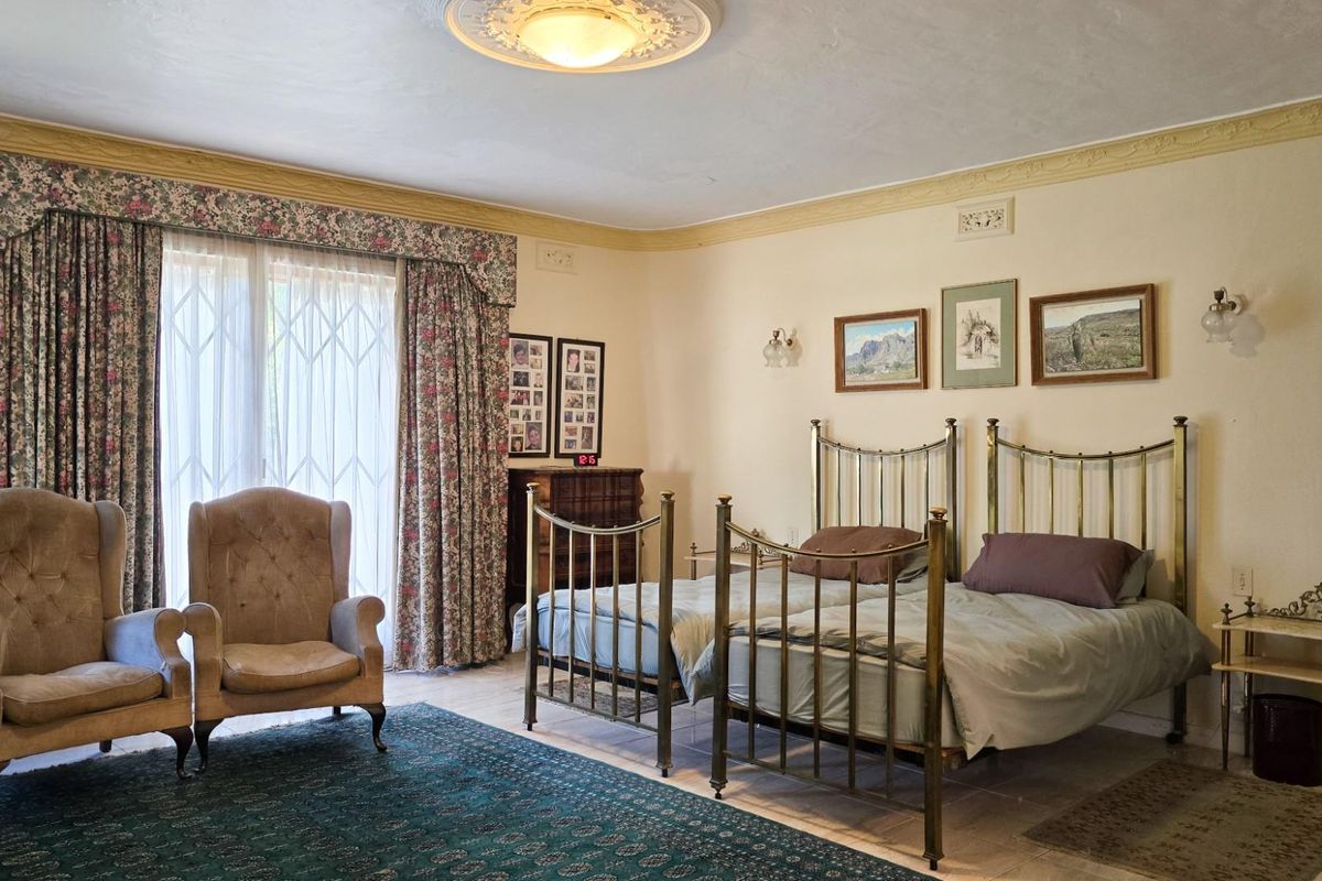 A spacious bedroom featuring tiled flooring, decorative ceiling rose, and sliding glass doors with security gates leading to the exterior.