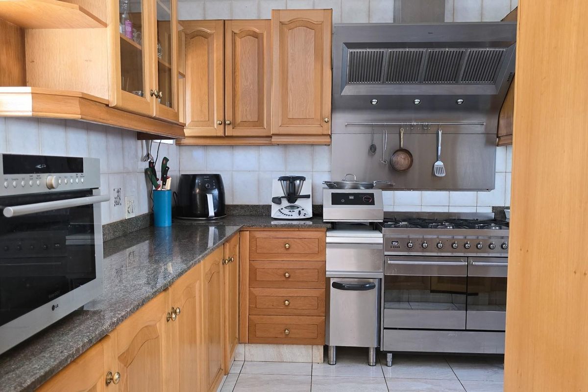 A functional kitchen featuring wooden cabinetry, granite countertops, a stainless steel gas range with extractor hood, and a built-in wall oven.