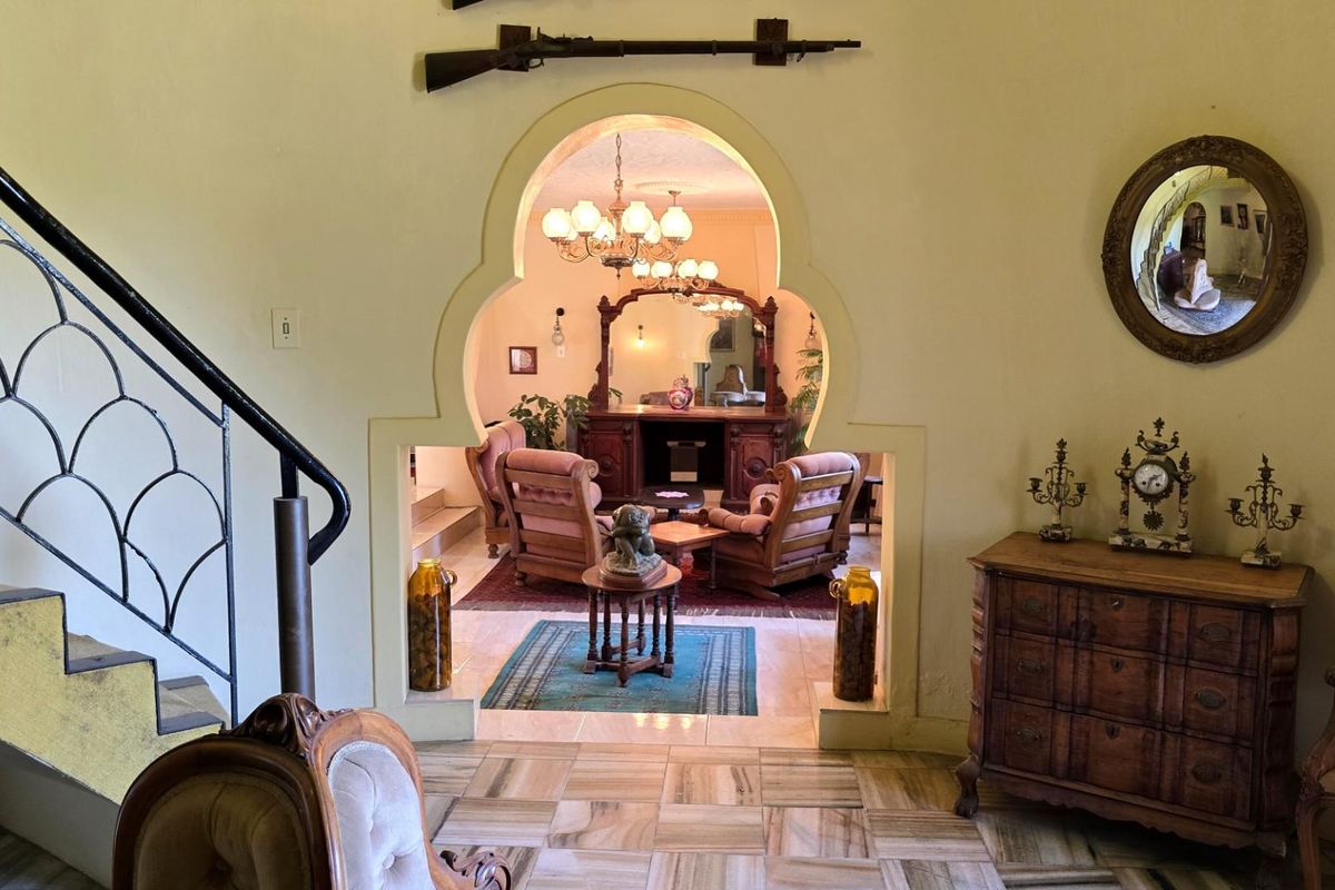 An interior view featuring a distinctive arched doorway leading into a living area, with tiled flooring and a staircase with a decorative metal railing.