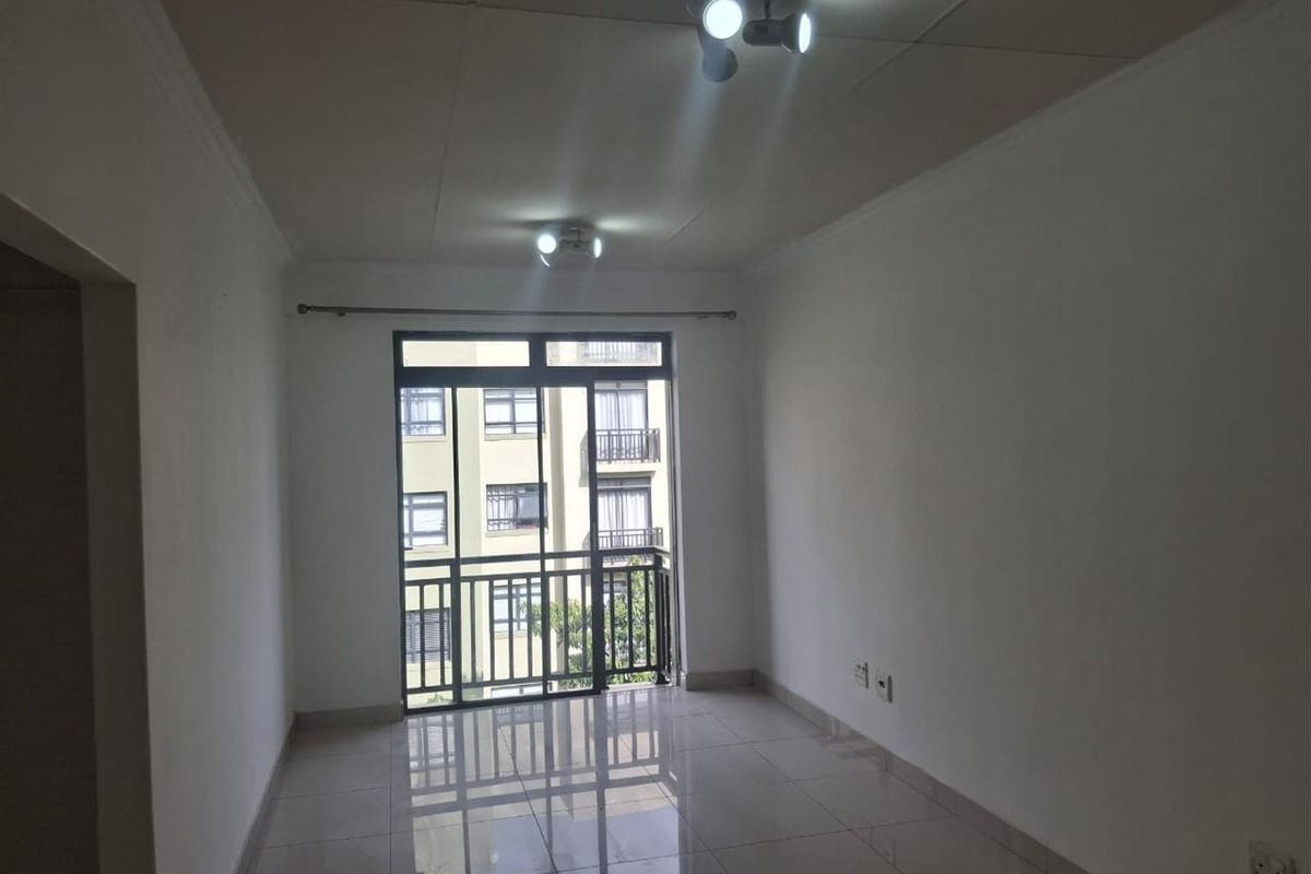 An empty living room featuring tiled flooring, ceiling-mounted lighting, and a sliding glass door leading to a balcony.