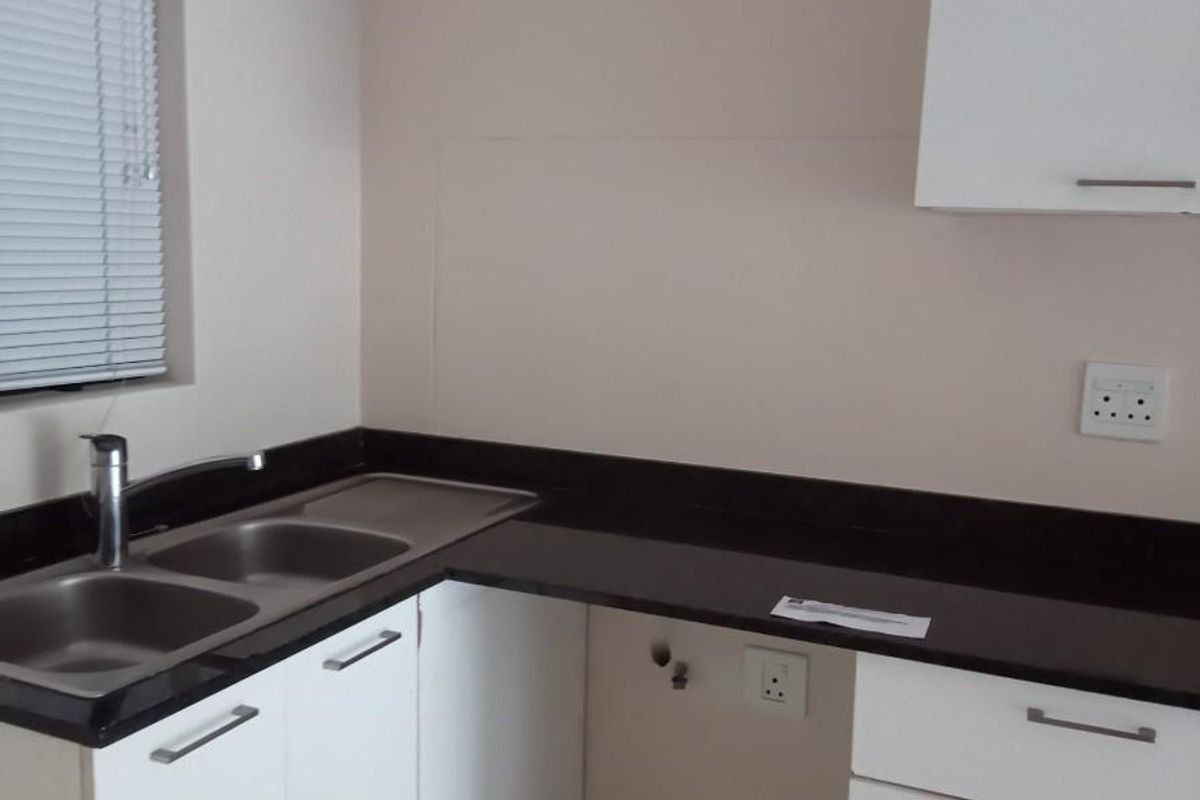 A functional kitchen area featuring white cabinetry, a dark stone countertop, a double stainless steel sink, and a dedicated space for an under-counter appliance.