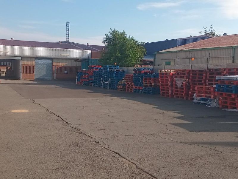 A commercial rear yard featuring asphalt paving, perimeter walling with electric fencing, and access to industrial warehouse structures with roller shutter doors.
