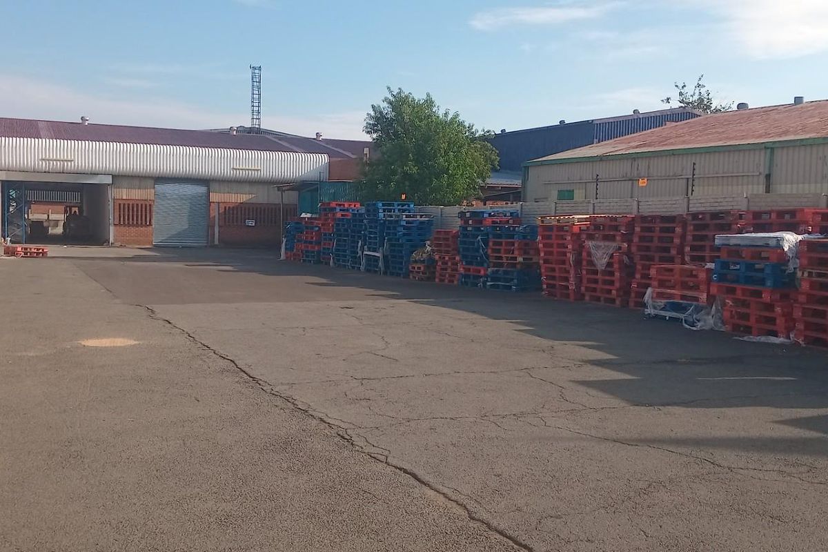 A commercial rear yard featuring asphalt paving, perimeter walling with electric fencing, and access to industrial warehouse structures with roller shutter doors.
