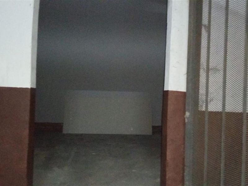 A dimly lit, vacant utility or storage space featuring concrete flooring and a secure metal gate entrance.