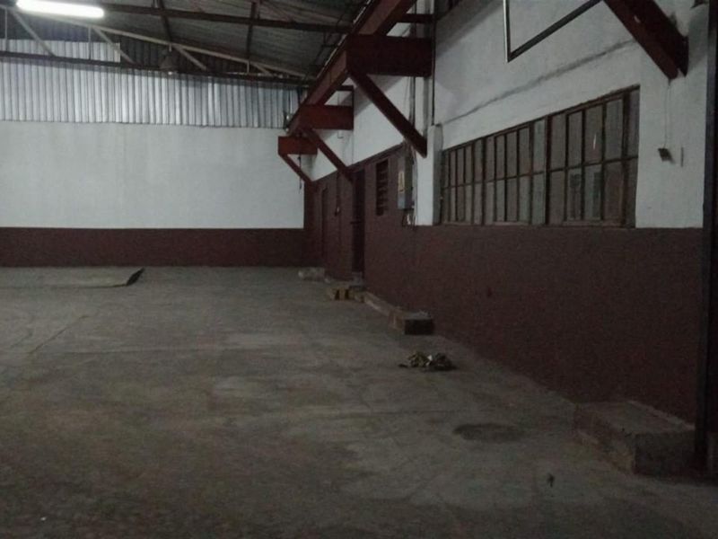 Spacious industrial utility area featuring exposed steel roof trusses, concrete flooring, and large steel-framed windows, suitable for warehouse or workshop use.