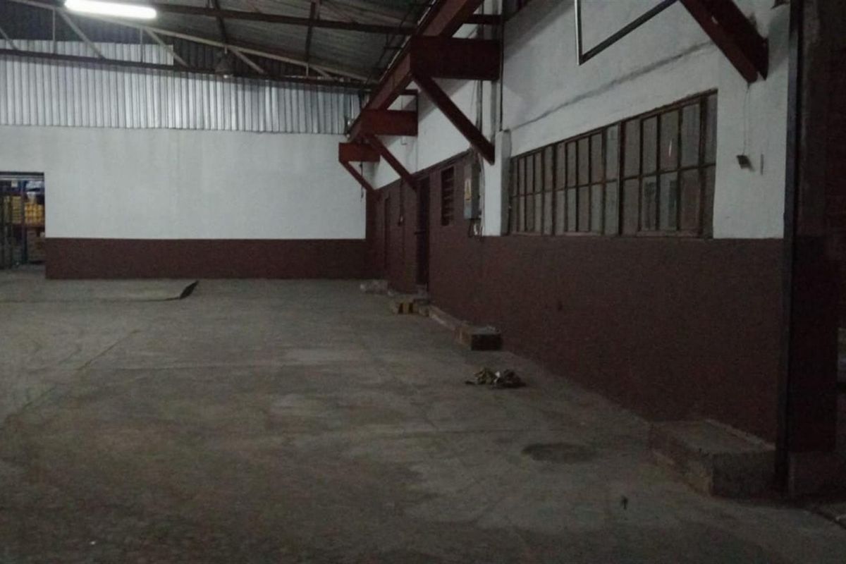 Spacious industrial utility area featuring exposed steel roof trusses, concrete flooring, and large steel-framed windows, suitable for warehouse or workshop use.