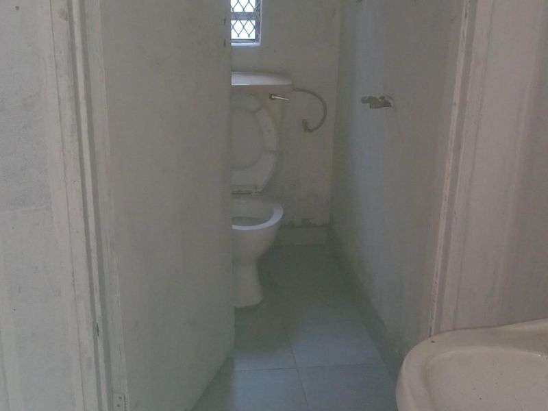 A basic commercial bathroom facility featuring multiple toilet stalls and a wall-mounted washbasin with dated finishes.