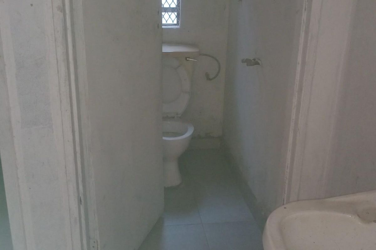 A basic commercial bathroom facility featuring multiple toilet stalls and a wall-mounted washbasin with dated finishes.