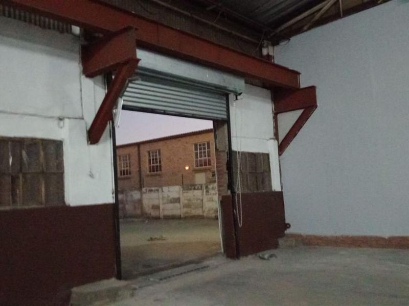 Empty industrial utility space featuring exposed steel structural beams, concrete flooring, and a large roller shutter door providing access to the exterior.