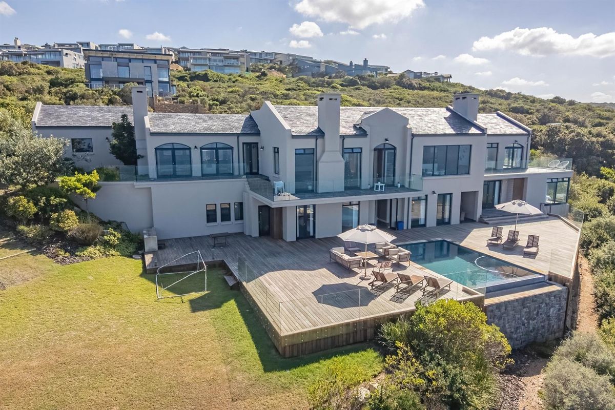 Aerial view of a luxury residence featuring a spacious timber deck, swimming pool, glass balustrades, and extensive rear garden area.