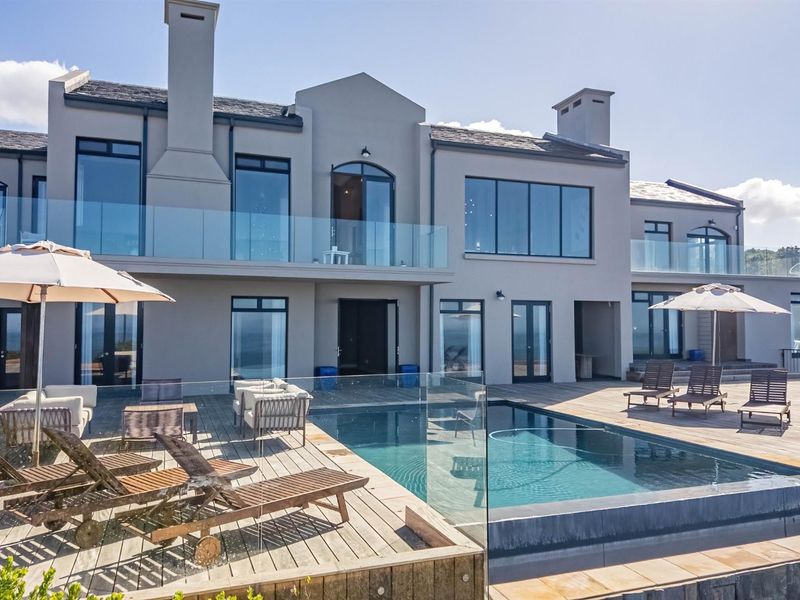 A luxurious rear exterior view featuring a swimming pool, expansive timber decking, glass balustrades, and a modern multi-story residence with large windows.