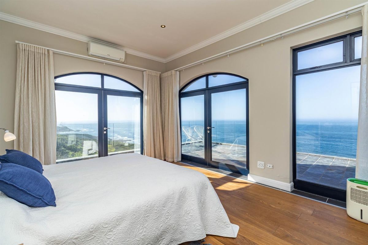 Spacious bedroom featuring hardwood flooring, crown molding, and expansive arched glass doors offering panoramic ocean views and direct access to an outdoor terrace.