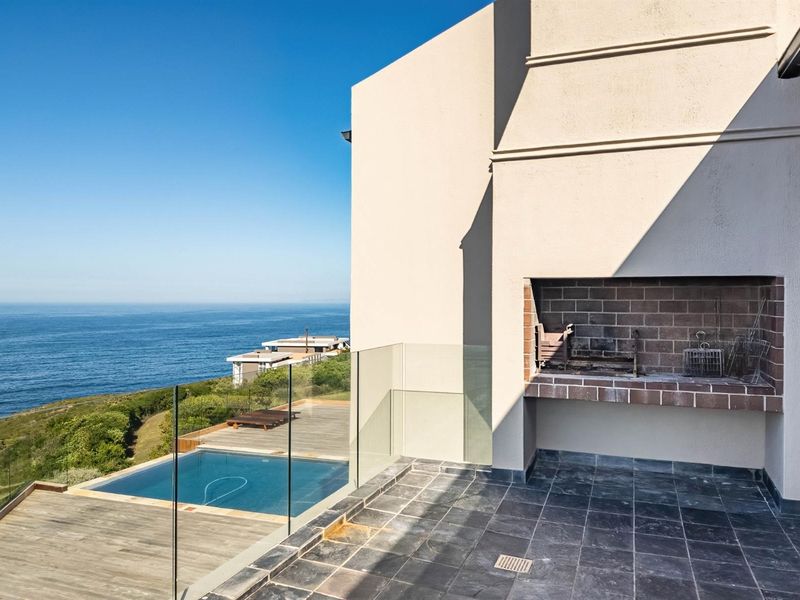 An elevated balcony featuring a built-in braai, glass balustrades, and tiled flooring, overlooking a swimming pool and scenic ocean views.