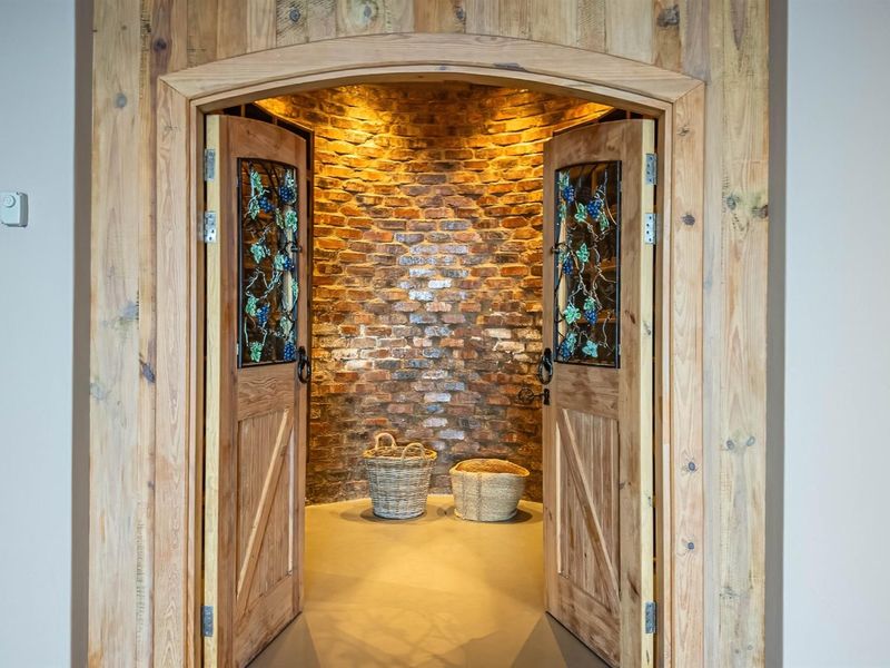A custom-built wine cellar featuring an arched timber entrance, decorative stained glass double doors, and a curved exposed brick interior wall.