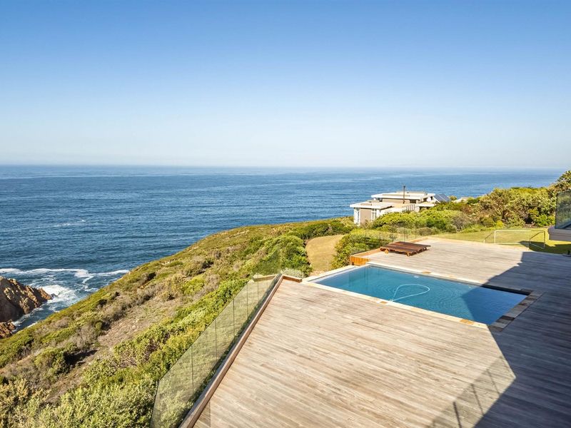 An elevated timber deck featuring a swimming pool with glass balustrades, offering expansive ocean views.