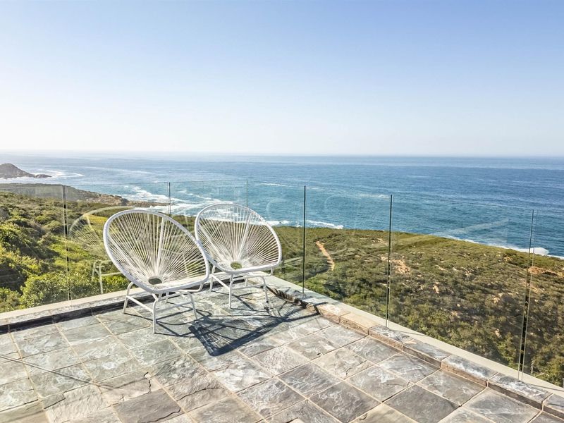 A modern balcony featuring stone tile flooring and a frameless glass balustrade, offering expansive, unobstructed ocean and coastal views.
