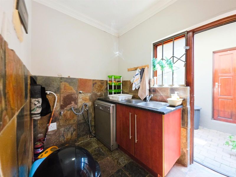 A functional scullery area featuring stone tile finishes, a double sink, and direct access to an outdoor space.