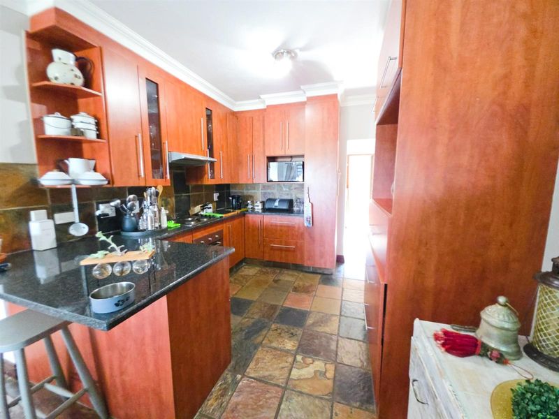 A functional kitchen featuring warm-toned wooden cabinetry, granite countertops, stone tile flooring, and integrated appliances including an extractor fan and microwave.