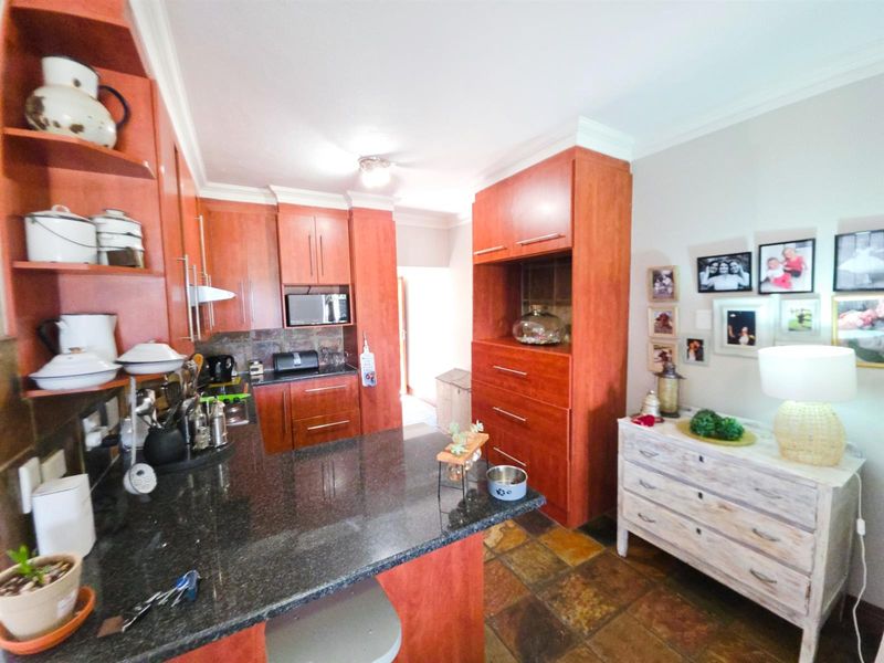 A functional kitchen featuring warm-toned wooden cabinetry, dark granite countertops, and durable stone tile flooring, offering ample storage and workspace.