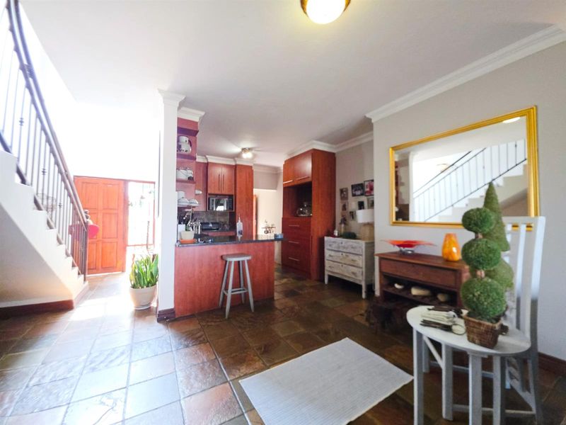 Open-plan living area featuring stone tile flooring, a built-in kitchen with breakfast bar, and a staircase with a decorative metal balustrade.