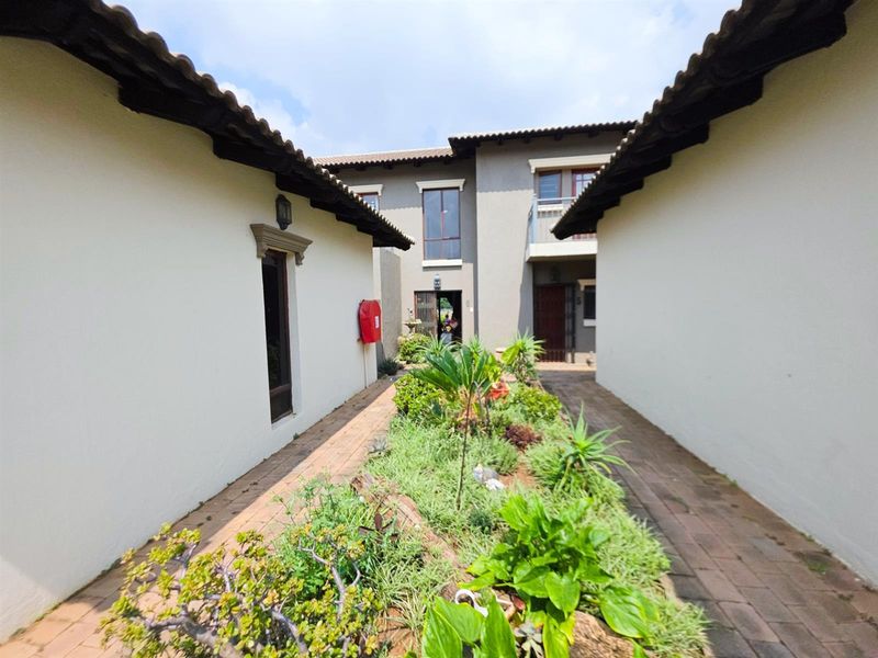 A view of the exterior courtyard area between townhouse units, featuring paved walkways, landscaped garden beds, and tiled roofing.