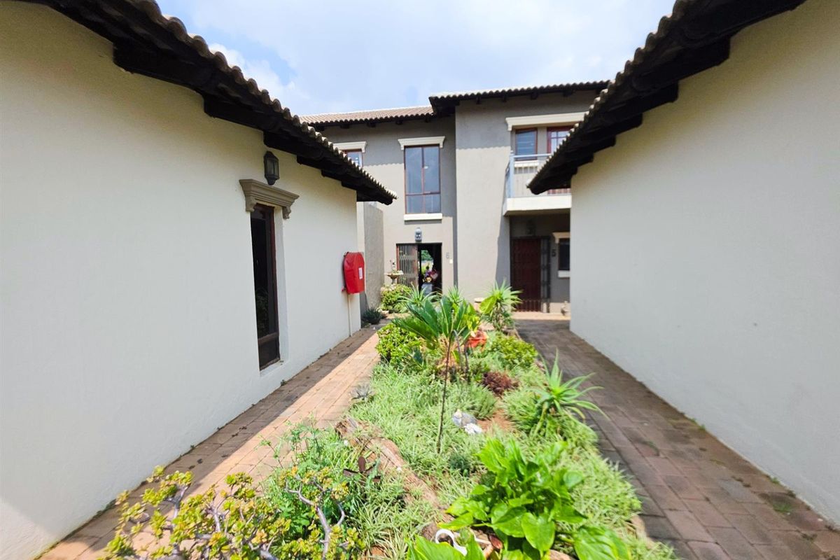 A view of the exterior courtyard area between townhouse units, featuring paved walkways, landscaped garden beds, and tiled roofing.