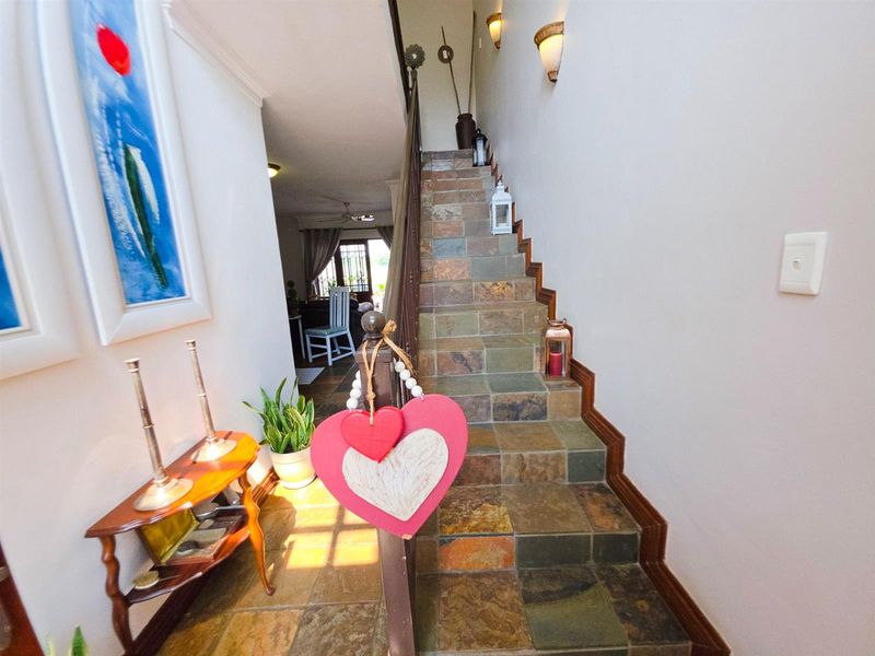 A hallway featuring a slate tile staircase with a wooden banister and wall-mounted sconce lighting, leading towards the living area.