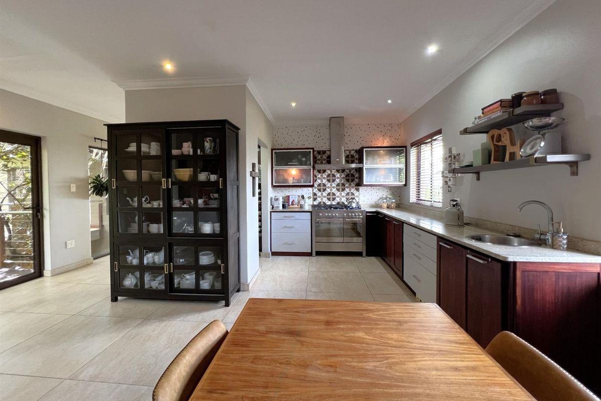 A well-appointed kitchen featuring stone countertops, a gas stove with stainless steel extractor, and ample built-in cabinetry with tiled flooring throughout.
