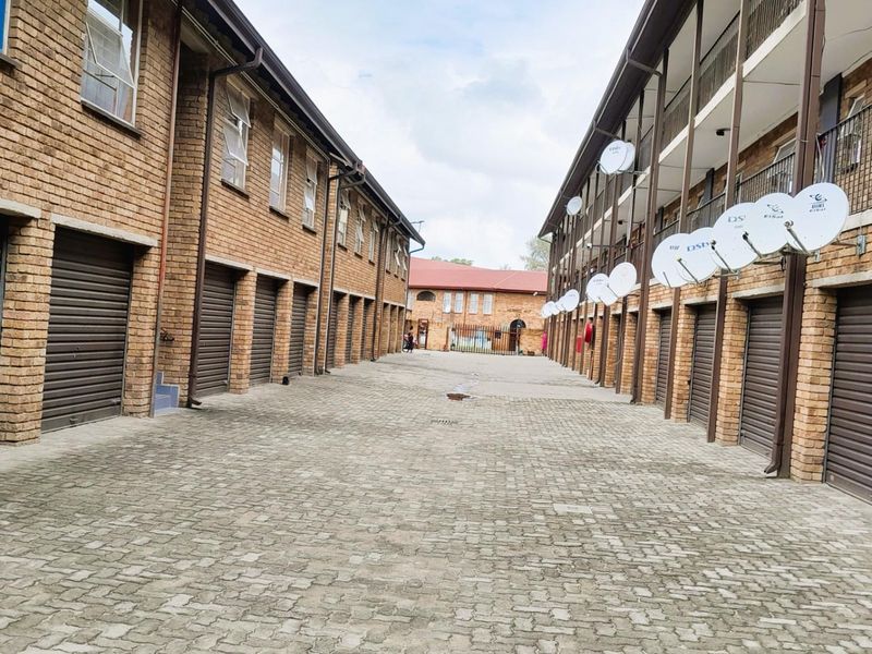 Exterior view of an apartment complex featuring a paved driveway, multiple roller shutter garage doors, and brick facade construction.