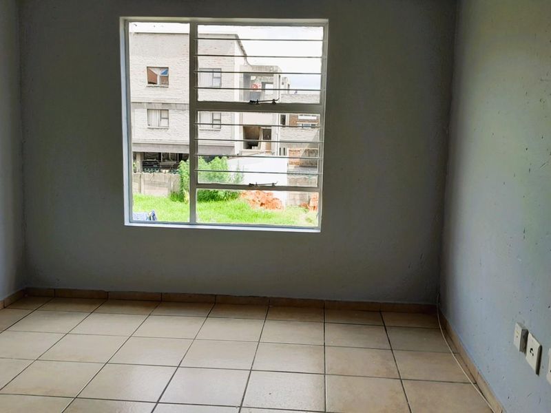 An empty bedroom featuring tiled flooring, a window with security bars, and neutral wall finishes, offering a blank canvas for personalization.
