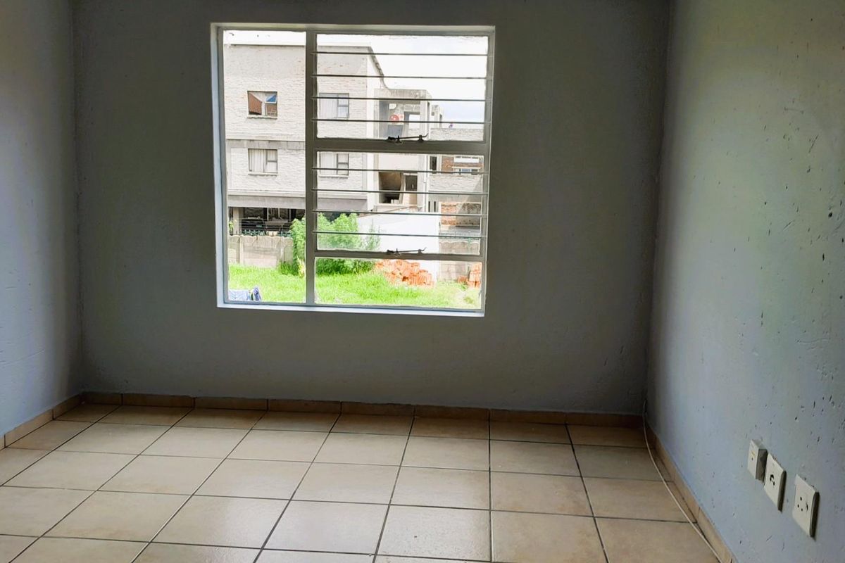 An empty bedroom featuring tiled flooring, a window with security bars, and neutral wall finishes, offering a blank canvas for personalization.