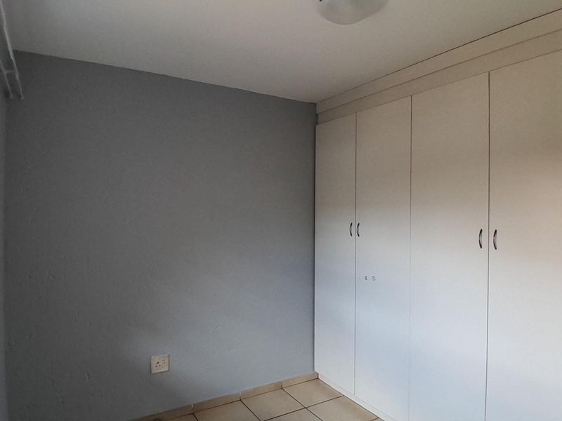 A clean, empty bedroom featuring neutral grey walls, tiled flooring, and ample built-in cupboard storage with security bars on the window.
