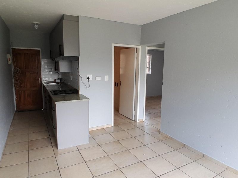 An open-plan living and kitchen area featuring tiled flooring, built-in cabinetry, and a fitted hob with an extractor fan.