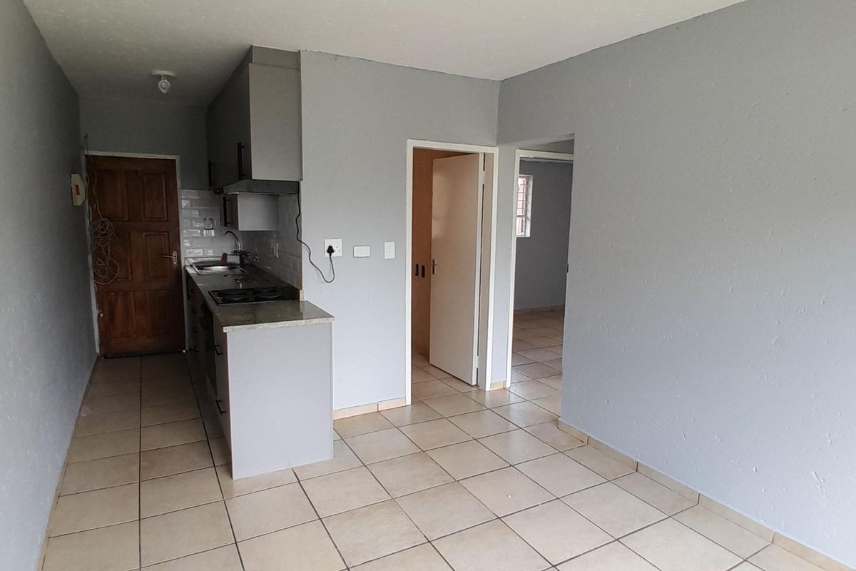 An open-plan living and kitchen area featuring tiled flooring, built-in cabinetry, and a fitted hob with an extractor fan.