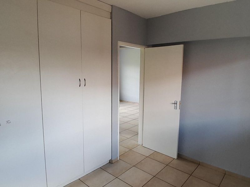 An empty bedroom featuring tiled flooring and built-in cupboards, with a doorway leading to an adjacent room.