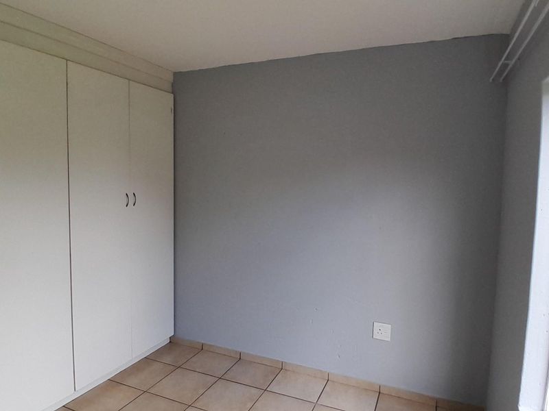 A clean, empty bedroom featuring neutral grey walls, tiled flooring, and ample built-in cupboard storage with natural light from the window.