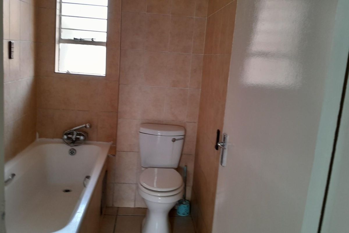 A functional bathroom featuring a standard bathtub, toilet, and tiled finishes, offering a clean and simple layout ready for potential modernization.