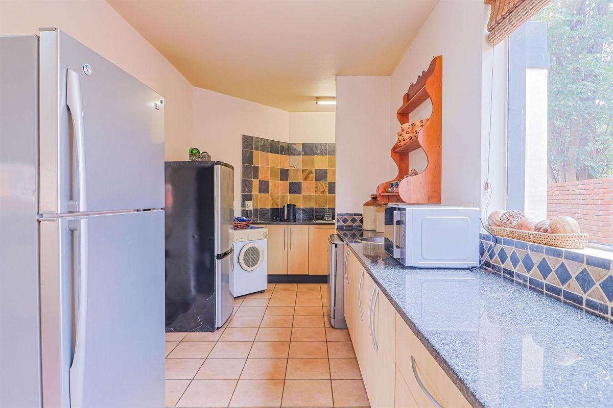A functional kitchen featuring granite countertops, light wood cabinetry, and a tiled splashback, with integrated space for laundry appliances.