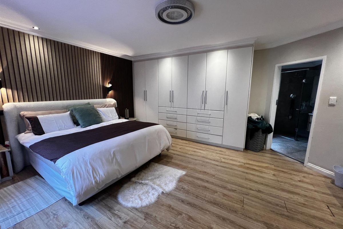 Spacious bedroom featuring modern wood-slat accent wall, extensive built-in cabinetry, and direct access to an en-suite bathroom.