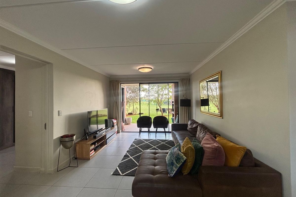 A well-maintained living room featuring neutral tiled flooring, ceiling cornices, and large sliding glass doors that provide direct access to the outdoor patio area.