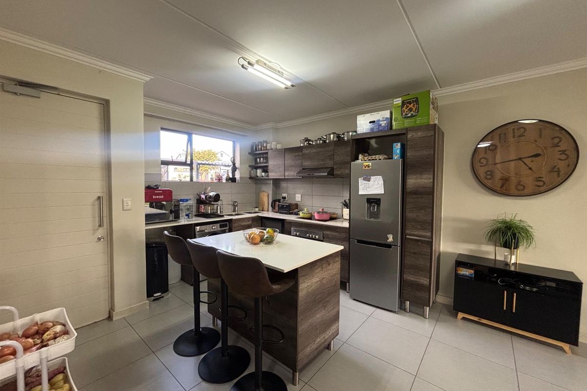 A functional kitchen featuring modern wood-look cabinetry, a central island with breakfast bar seating, tiled flooring, and integrated storage solutions.