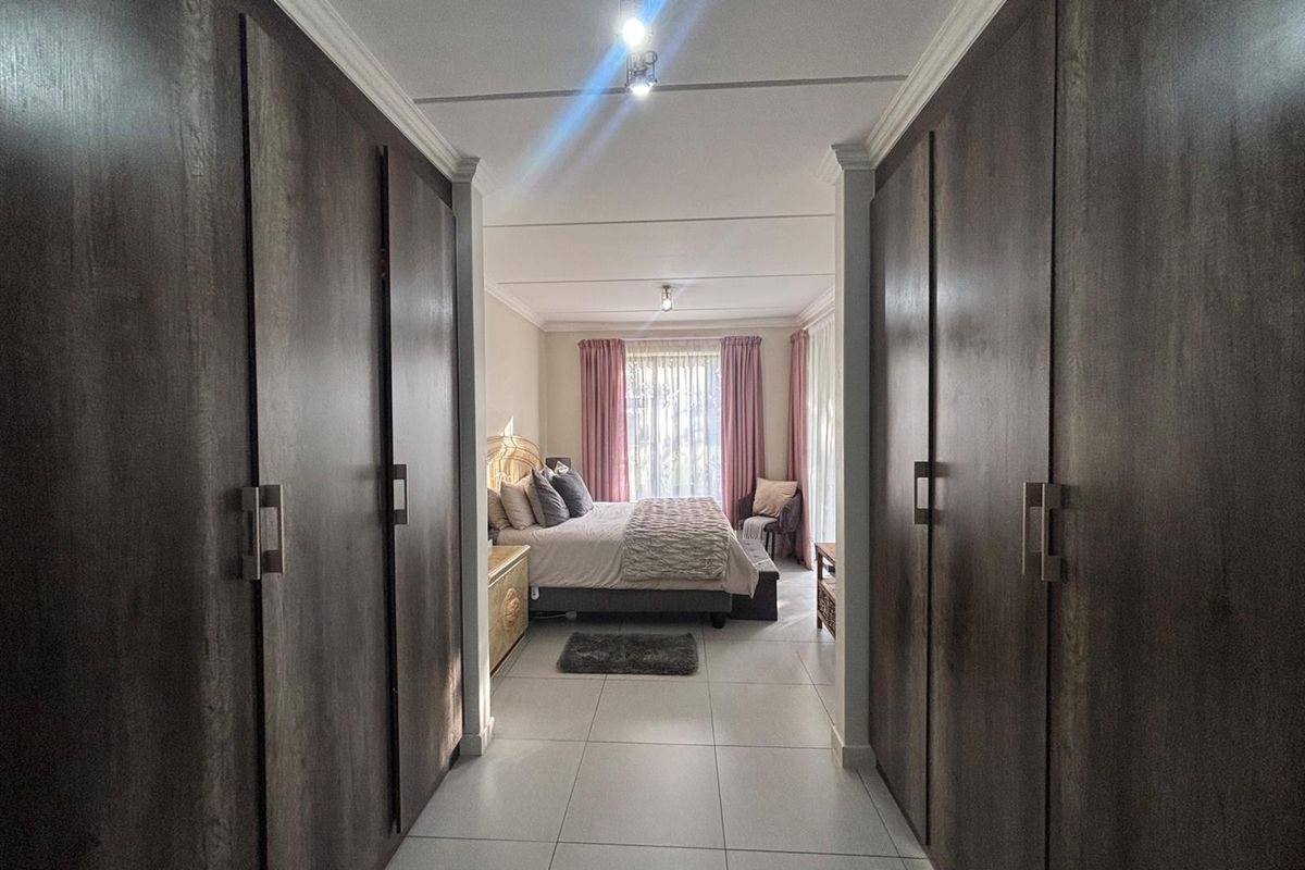 A bedroom featuring extensive built-in cupboards along the hallway entrance, tiled flooring, and natural light flowing from the window.