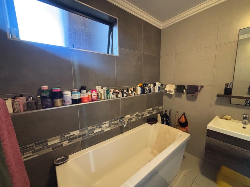 Modern bathroom featuring a built-in bathtub, wall-mounted vanity, and tiled finishes with a convenient recessed storage shelf.