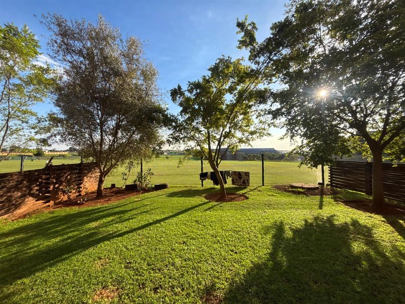 A well-maintained private garden featuring a lush lawn, mature trees, and secure perimeter fencing with views of an open field.