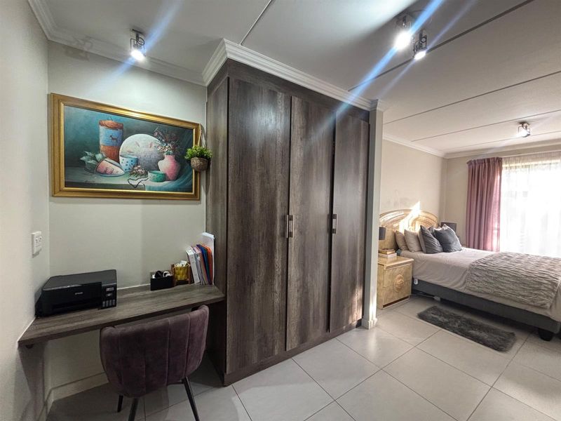A bedroom featuring a built-in wardrobe, integrated desk space, tiled flooring, and modern spotlight lighting.